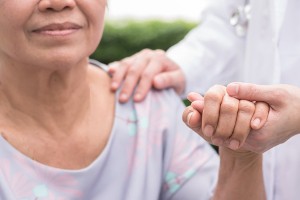 Elderly senior patient (aging old adult person) in nursing hospice home holding geriatrician doctor's hand having happy medical health care from hospital carer or caregiver healthcare service