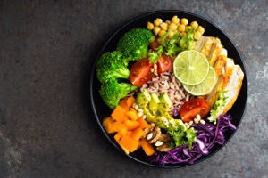 Buddha bowl meal with chicken fillet, brown rice, avocado, pepper, tomato, broccoli, red cabbage, chickpea, fresh lettuce salad, pine nuts and walnuts. Healthy balanced eating. Overhead view