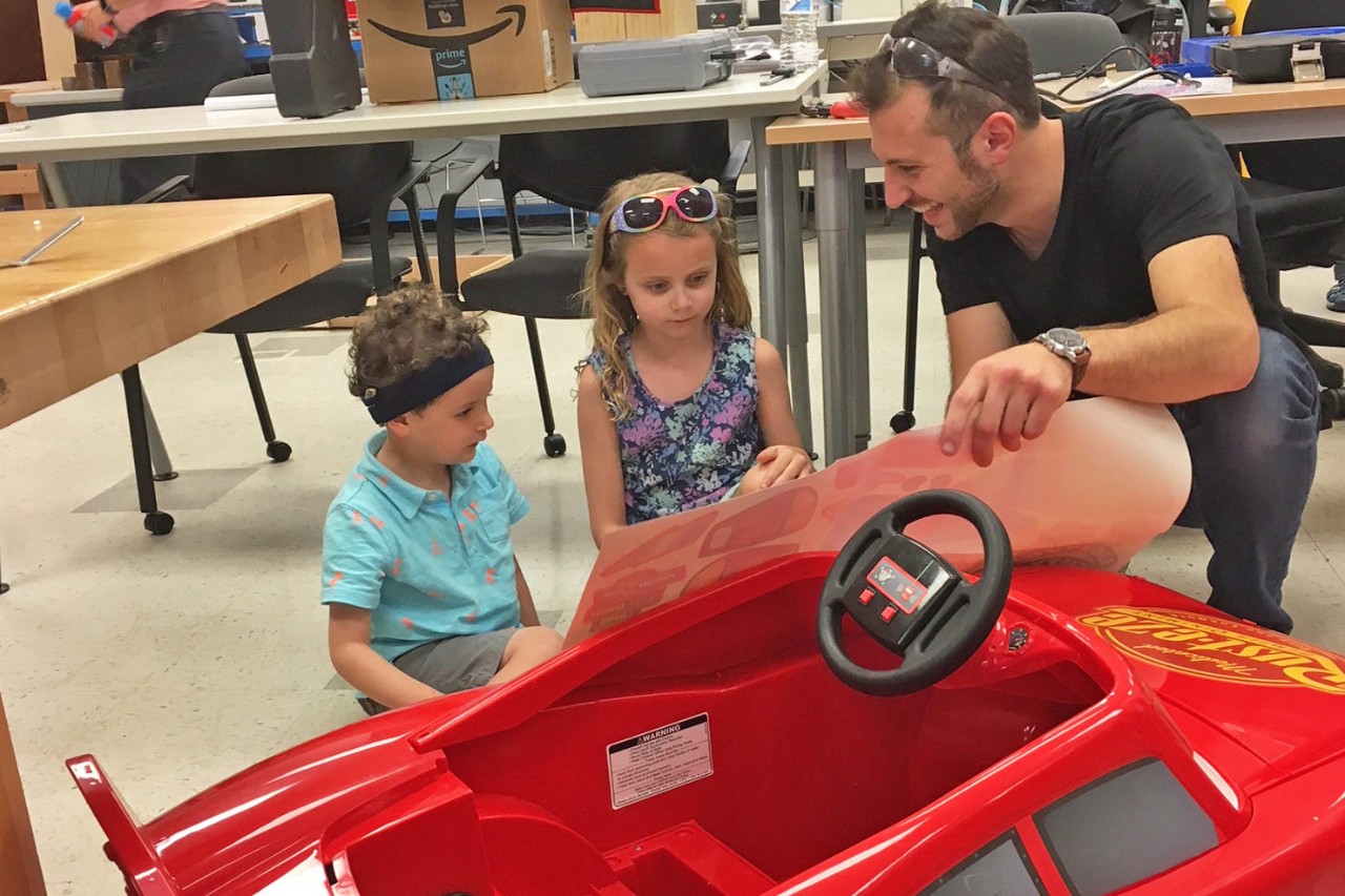 Student working on the design of a car with some help from children