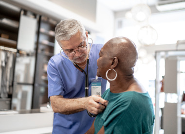 Black woman having her lungs checked by stethescope by a white physician in a doctor's office