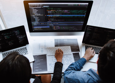 Woman and man working on artificial intelligence coding project for healthcare, sitting in front of three computer monitors