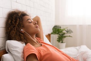 African-american woman relaxing and listening to music, lying in bed in the morning