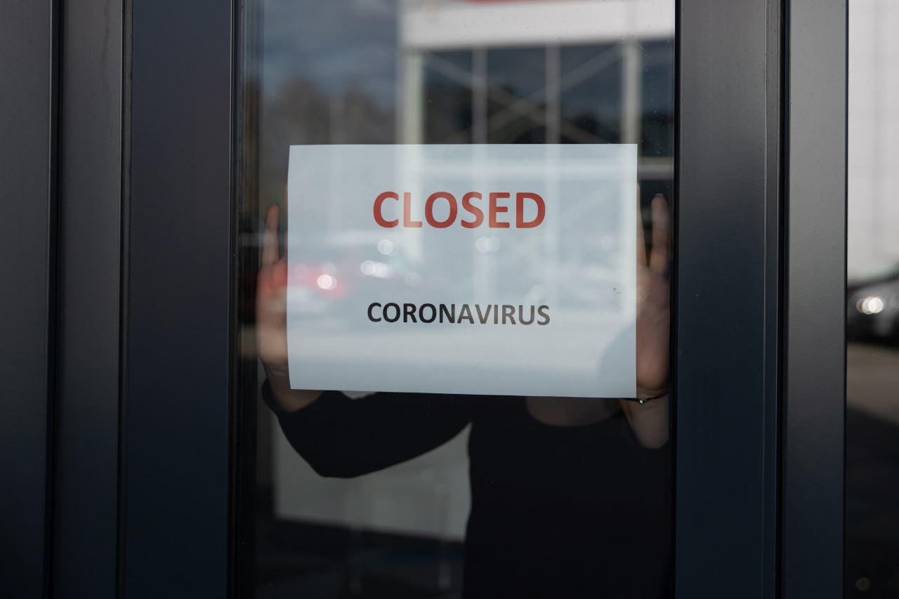 Woman hangs a card with information about the store closing on a shop window due to the coronavirus