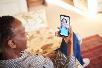 Senior African American woman using a smart phone app to consult with a doctor in real time while standing at home