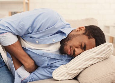 African-american man suffering from stomach ache, lying on sofa at home, closeup