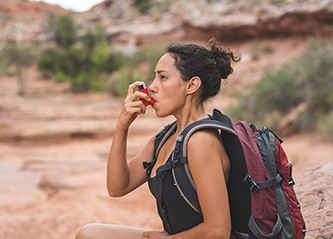 A young ethnic female takes a short break from her day hike in the Utah desert to use her inhaler.