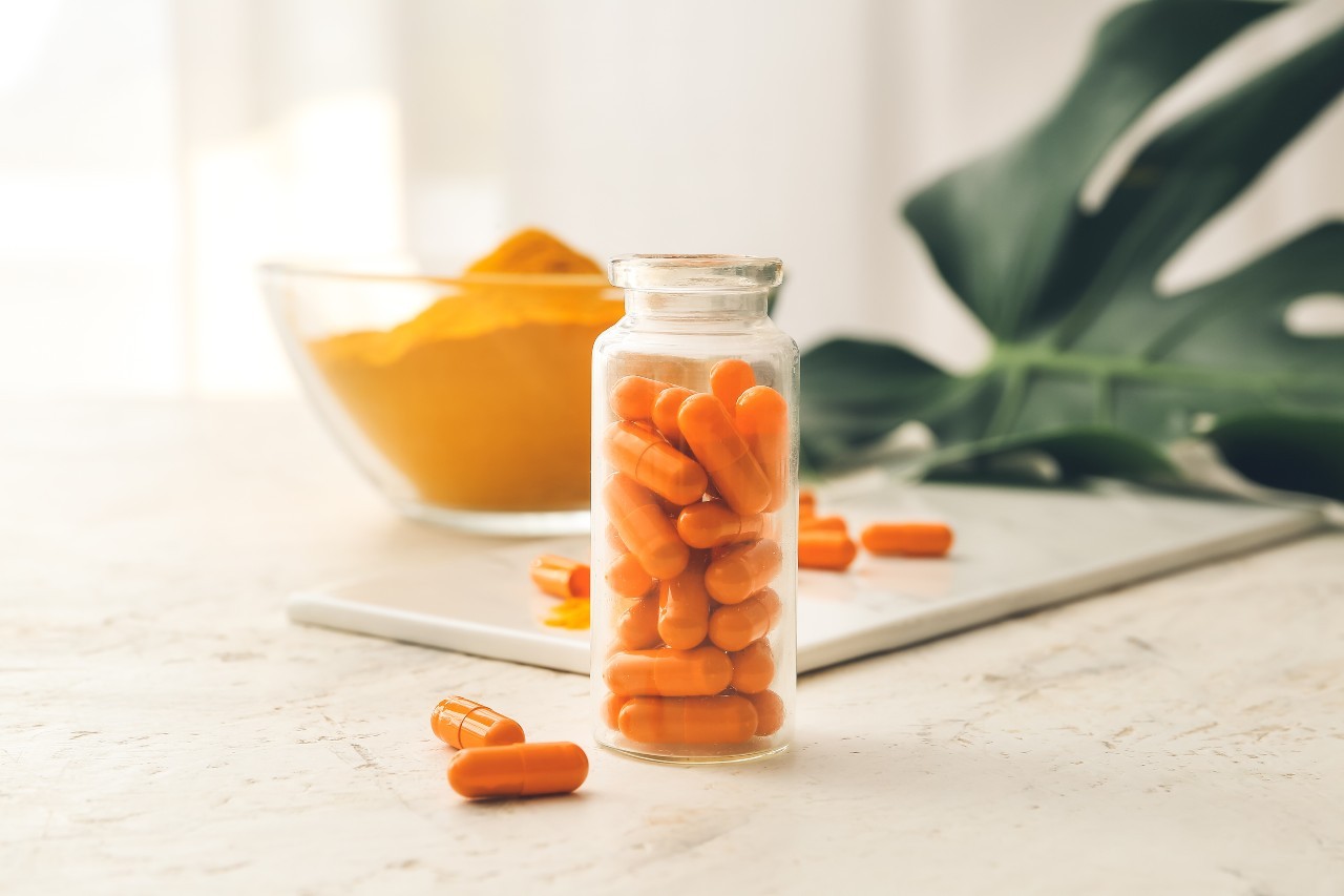 Bottle with turmeric pills on light background