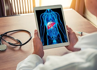 Doctor holding a digital tablet with x-ray of body skeleton with liver. Stethoscope and syringe on the desk