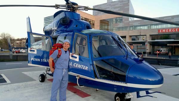 Perfusion student Kyle stands in front of a helicopter outside of a hospital emergency room.