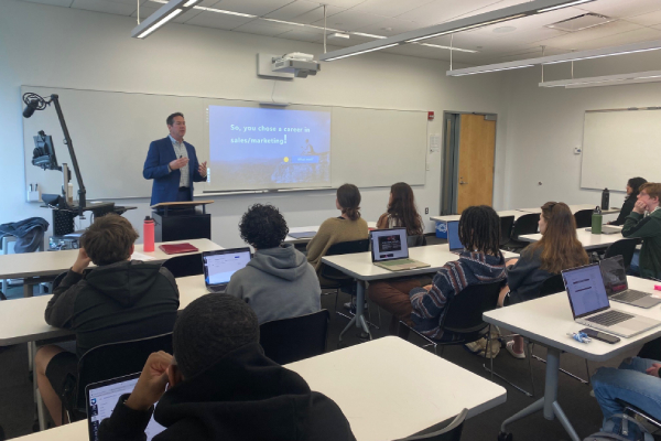 Male professional guest speaking in front of classroom of students.