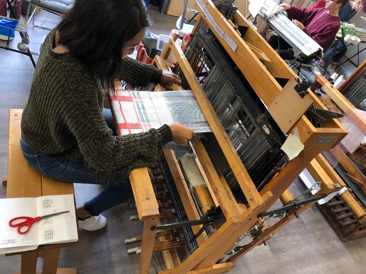 A student creating fabric on textile machine 