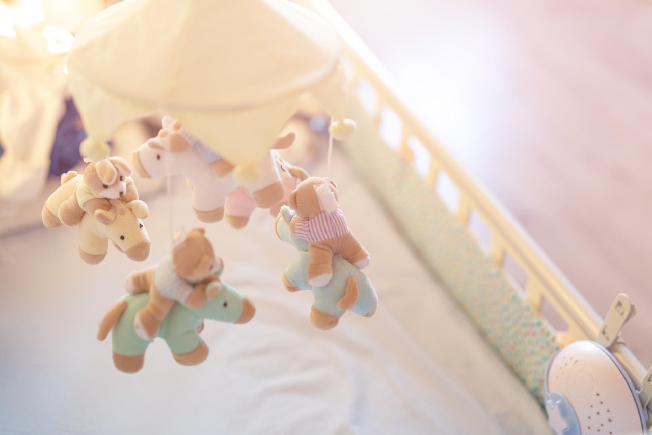 Close-up baby crib with musical animal mobile at nursery room. Hanged developing toy with plush fluffy animals. Happy parenting and childhood, expectation delivery of a child concept.
