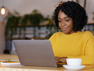 Female entrepreneur chatting with clients on laptop, drinking coffee and working at cafe, empty space
