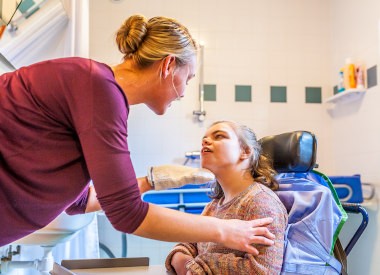 A disabled child in a wheelchair being cared for by a nurse in the bathroom.