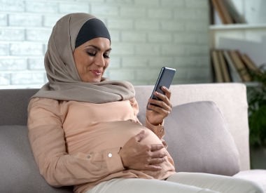 Muslim pregnant female watching video on smartphone home, expecting childbirth