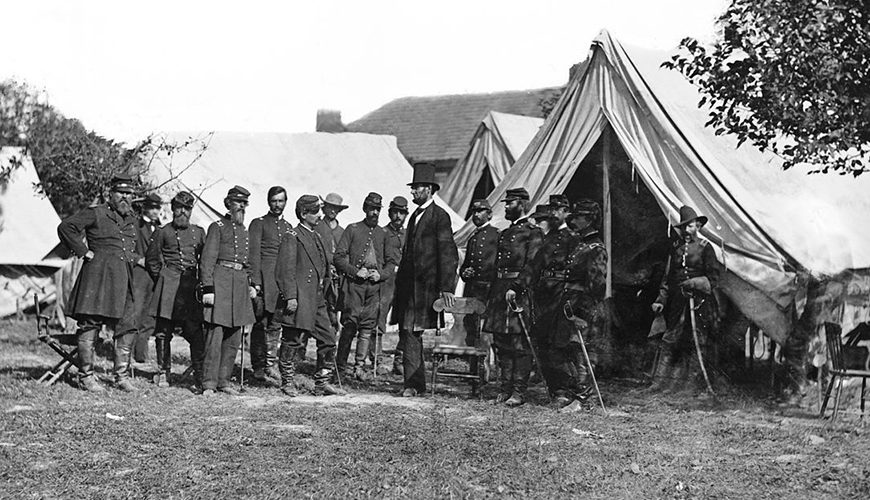Old photograph of soldiers standing in front of tents.