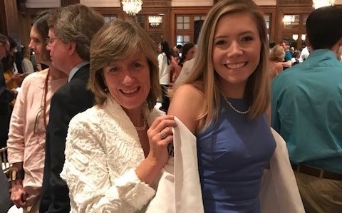 This image shows Patricia Curtin White, MD, putting a white doctor's coat on her daughter Mary White, MD, at a graduation ceremony.