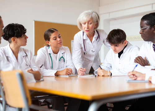 Elderly female doctor conducts training for interns of different ages at round table in auditorium of medical university