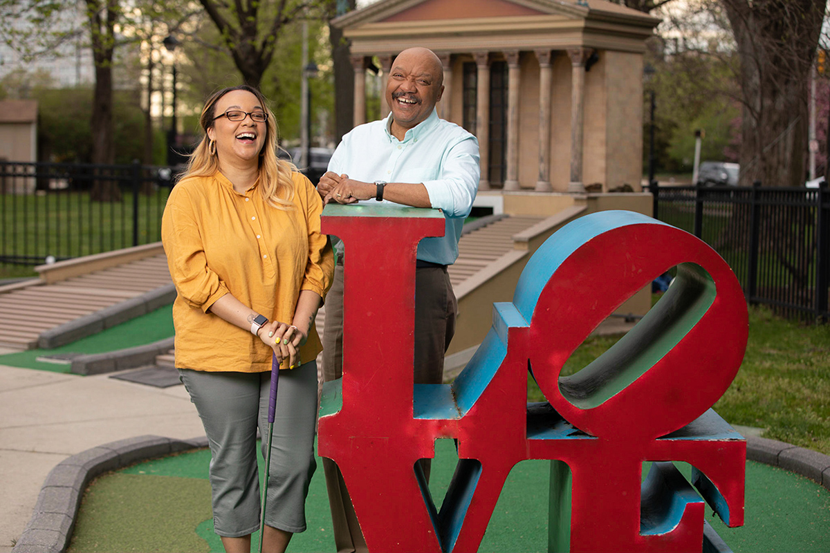 Nicole standing with her father next to miniature love statue.