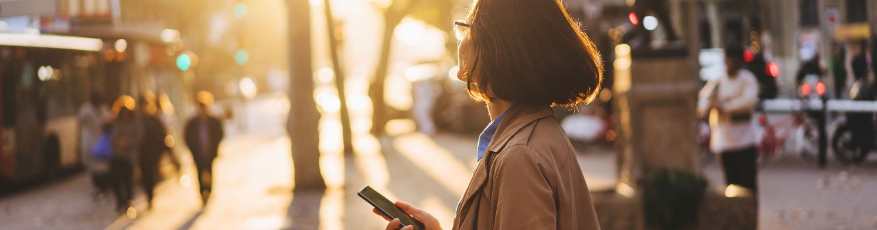 Girl enjoying sunset and chatting with friends via smartphone on the city streets