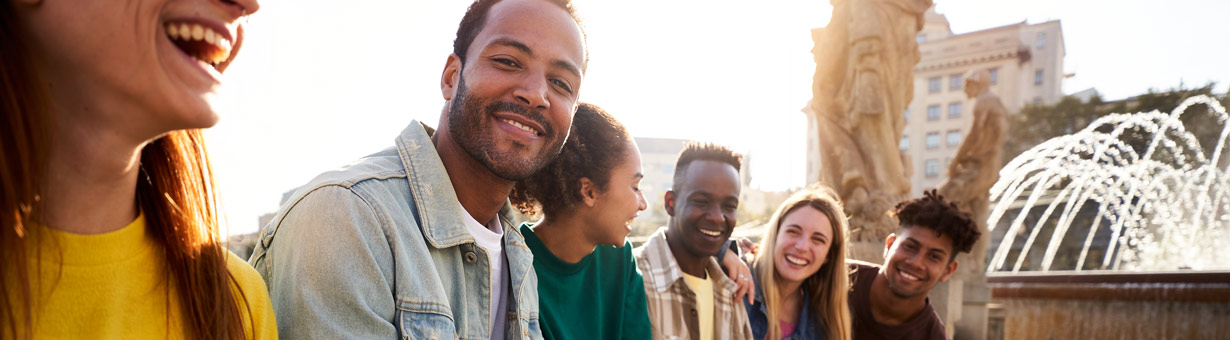 Side view of group of Erasmus people ganging out outdoors having fun, one guy looking at camera smiling. Copy space.
