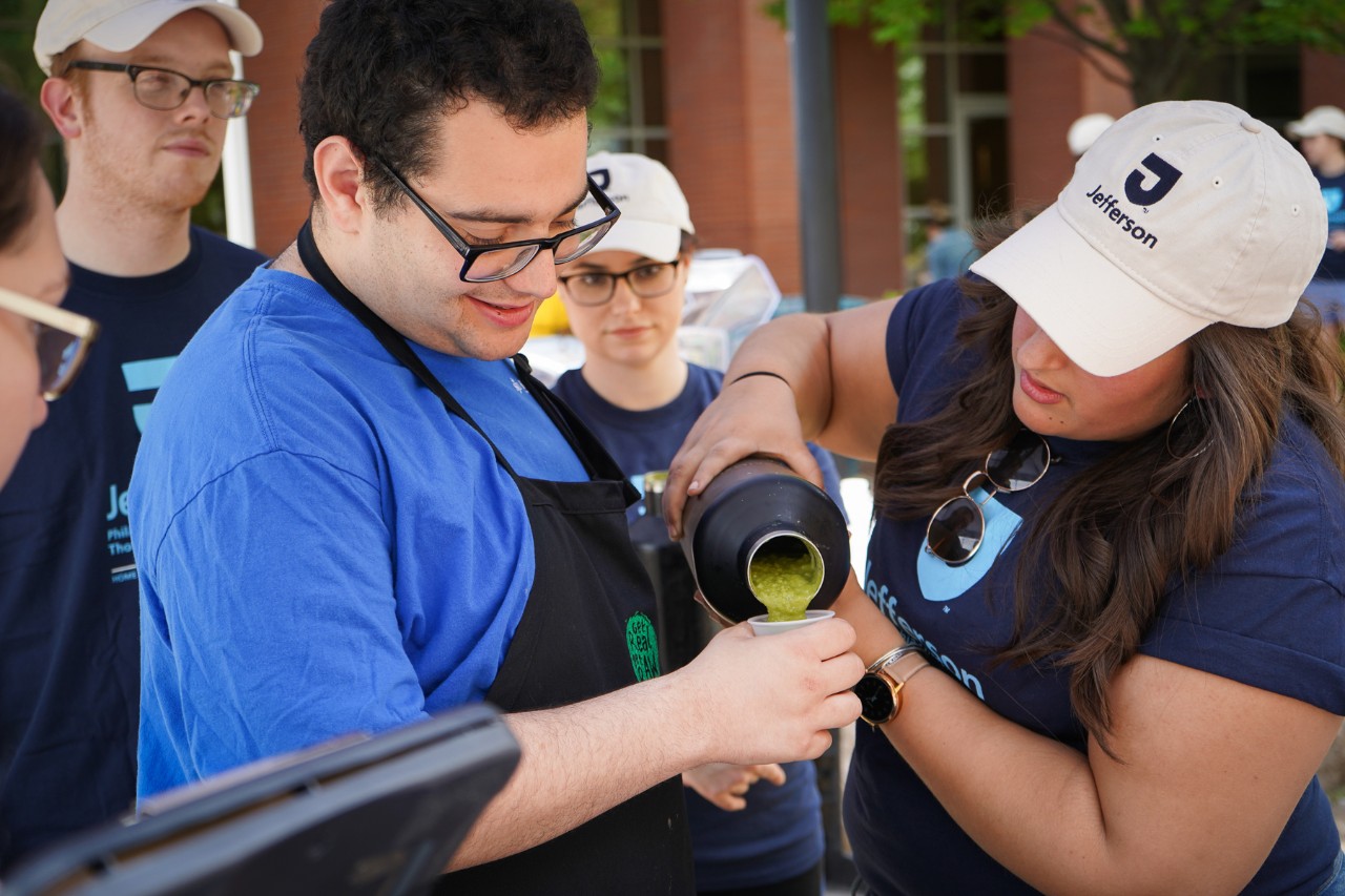 An OT student pours out a smoothie into a cup held by Adam Miller.