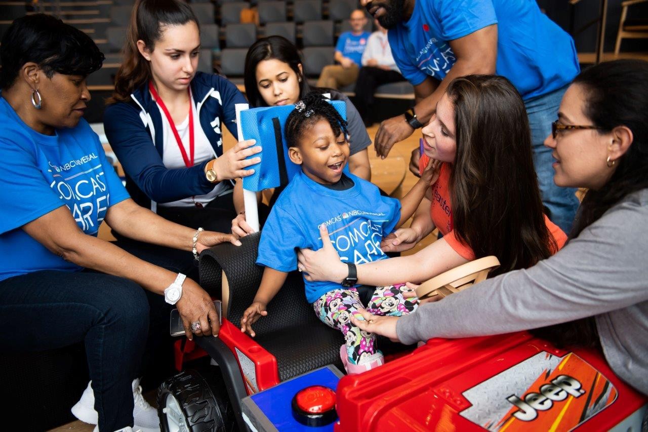 Students place a young child into a toy car.