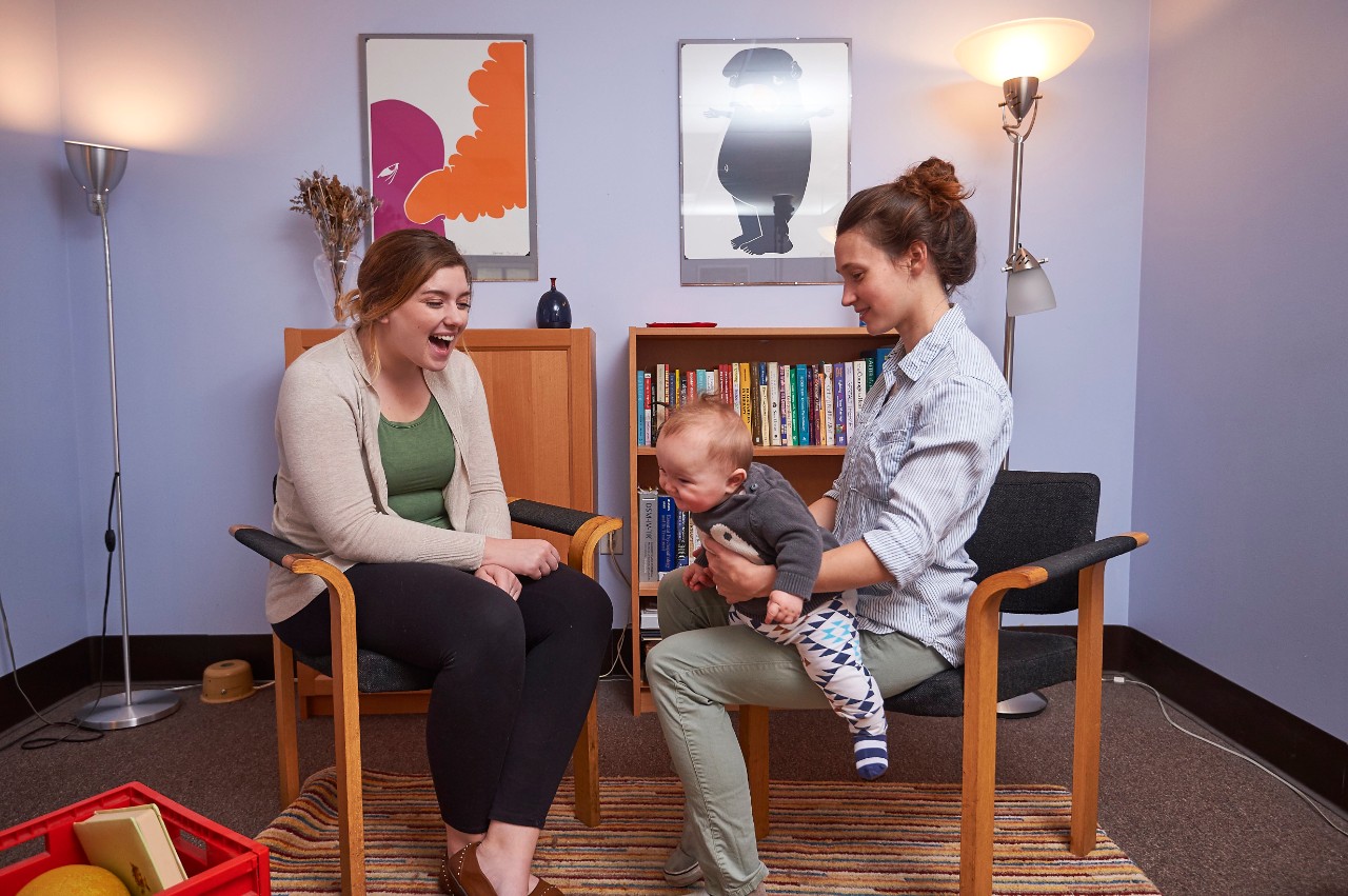 Two women talking and sitting in chairs. A baby on the lap of one.