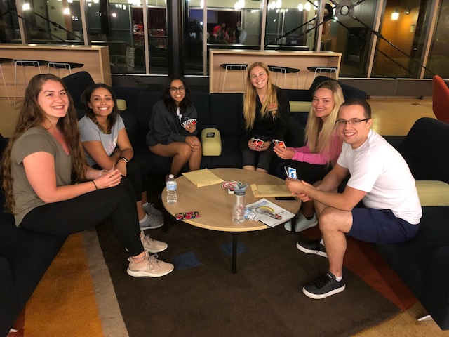 Six students sit around a table playing cards.