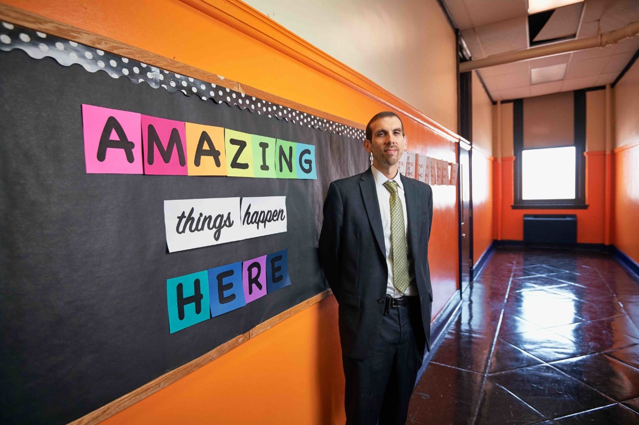 The principal stands in front a bulletin board that reads amazing things happen here