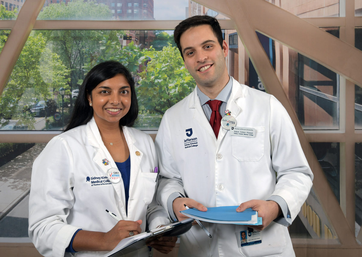 Two medical students- one holding a voting clipboard, the other a folder.