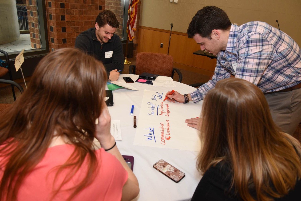 four students sit around a table working on a project