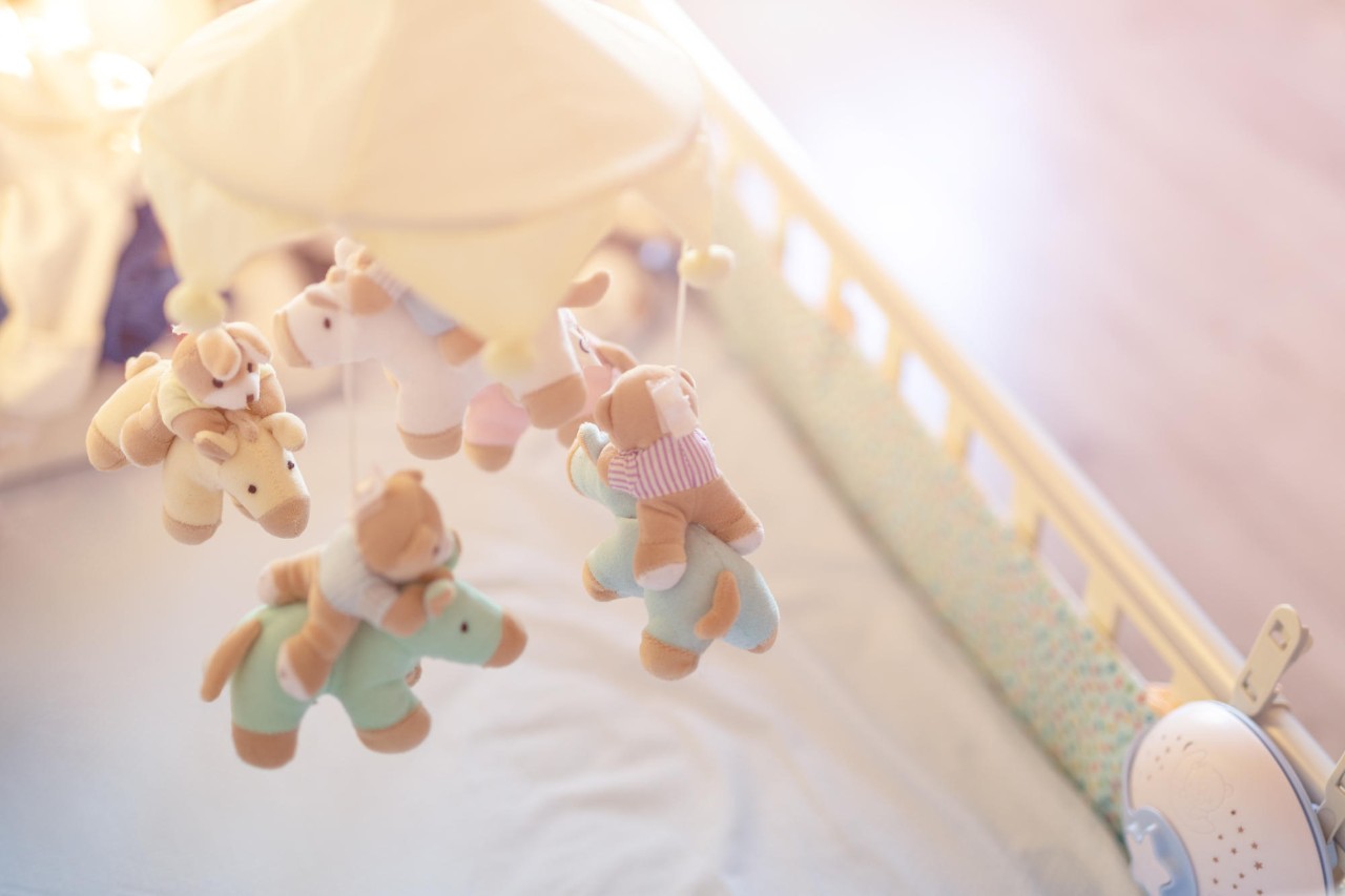 Close-up baby crib with musical animal mobile at nursery room. Hanged developing toy with plush fluffy animals. Happy parenting and childhood, expectation delivery of a child concept