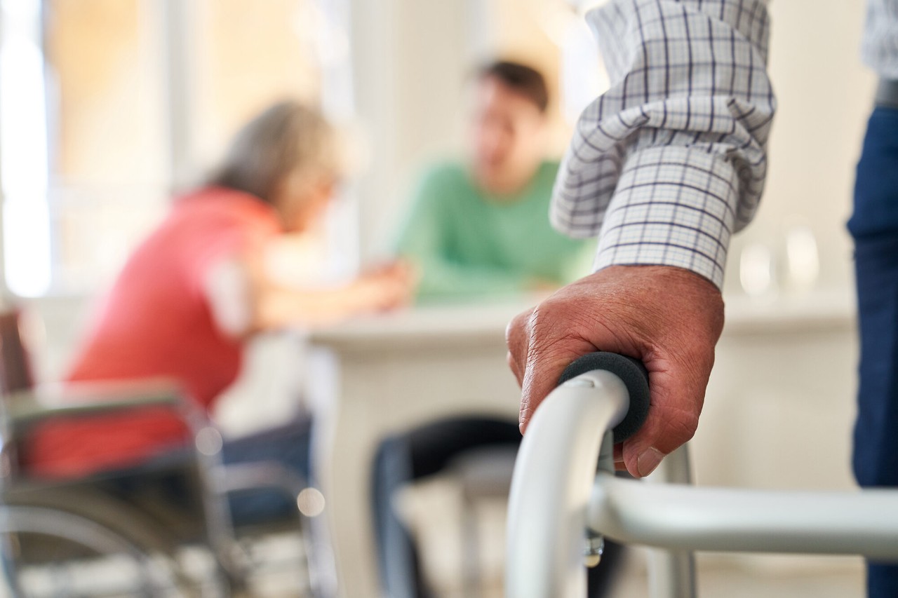 hand on a walker with two white people sitting at a table in the background.