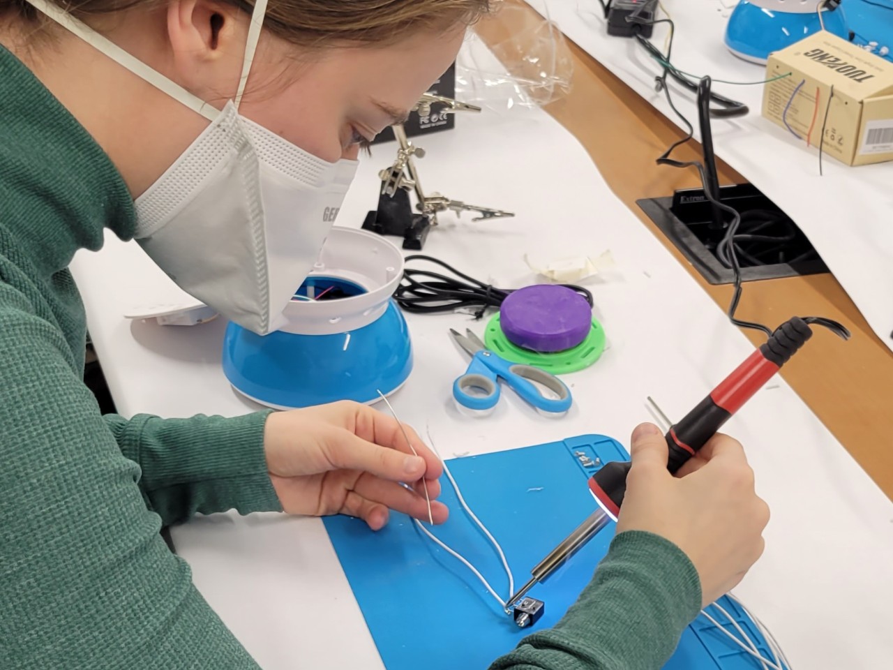 An occupational therapy student solders components necessary to make a toy accessible to a child with a disability.